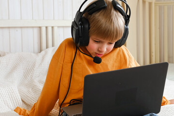 Little smiling 6 years old boy using a laptop with headphones. Child having video call with...
