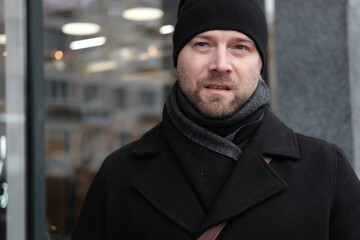 Handsome man wearing black coat and brown leather bag walking down on the city with mobile phone in hand. Stylish bearded middle-aged male using smartphone at urban street. Businessman going on job.