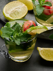 Refreshing mojito cocktail with lime, mint, strawberry, and ice on dark background