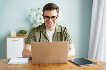 Focused young man working on his laptop at a cozy modern workspace surrounded by greenery and...