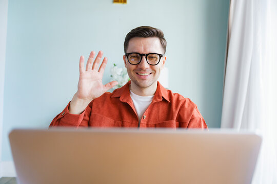 Smiling man waves from his home office during a virtual meeting while showcasing a relaxed and friendly atmosphere