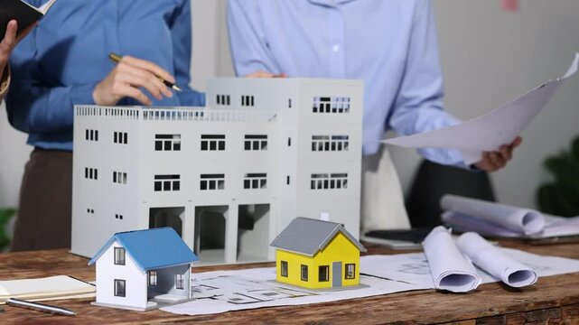 Professional architects examining blueprints and discussing sustainable building project with miniature model, emphasizing eco-friendly design and urban planning.
