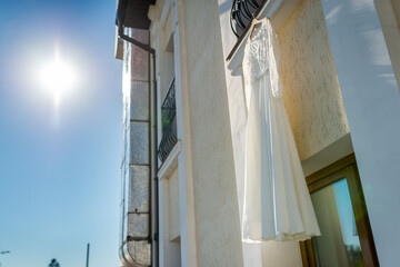 Dress hanging outside a modern building. A wedding dress dangles from a balcony under a bright sun,...