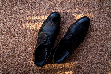 Elegant black dress shoes on a carpet. Shiny black dress shoes sit on a textured carpet in a well-lit room, highlighting their polished finish and details.