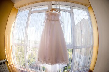 Wedding dress hanging in bright sunlight. A beautiful wedding dress is displayed by a window,...