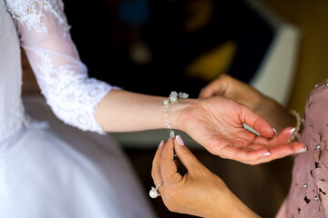 Bride wears bracelet pre-ceremony. A bride is having a delicate bracelet fastened by a friend or...