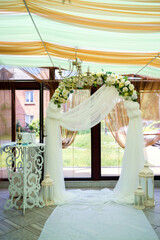 Floral wedding arch. Floral archway set up indoors for a wedding ceremony, featuring draping fabric and ambient lighting.