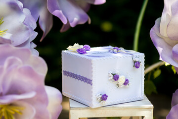 Beautifully decorated gift box in garden. A lavender gift box adorned with floral designs sits among large, colorful flowers in a serene garden setting.