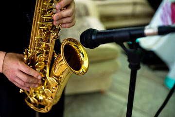 Saxophonist plays at venue. A musician plays a golden saxophone while standing near a microphone in a lively indoor setting.