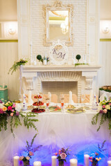 Elegant wedding reception table decor. A decorated table with flowers and treats by a white fireplace sets a romantic wedding reception ambiance.