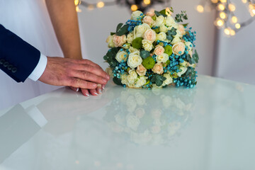 Couple's hands beside wedding bouquet. A couple's hands touch gently on a table near a beautiful wedding bouquet during their celebration.