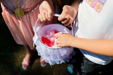 Kids having fun treasure hunting. Two children hold a decorated basket filled with colorful petals during a playful outdoor activity on a sunny day.