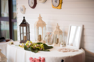 Lanterns and flowers on table. A charming table features decorative lanterns, a floral arrangement, and a blank frame in a cozy, inviting space.