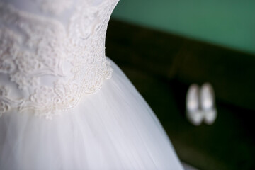 Delicate lace details on a bridal gown. Intricate lace embellishments adorn the waist of a wedding dress, with elegant shoes placed nearby in soft light.