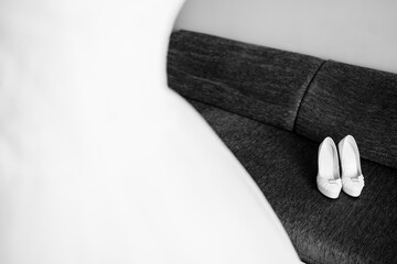 Shoes by gown on couch. White bridal shoes rest on a couch near a flowing wedding gown, capturing a...