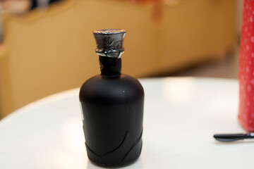 Black bottle with metallic lid. A distinctive black bottle sits on a white table, featuring a shiny...
