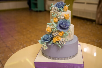 Floral wedding cake design. Three-tiered cake adorned with blue and yellow flowers, showcasing elegant design at a wedding celebration.