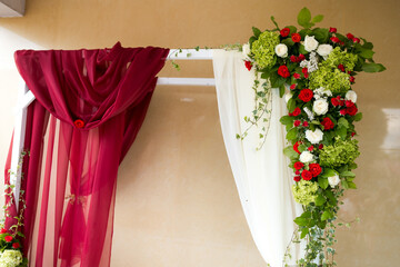 Wedding entrance floral decor. Richly adorned entrance decorated with vibrant flowers in red, white, and green hues. Elegant drapes frame the setting.