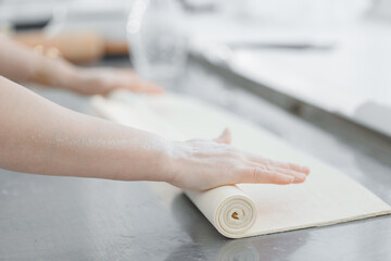 Baker rolling dough on metal table in bakery factory