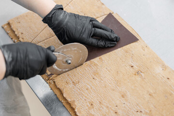 Caucasian female adult using pizza cutter on pastry dough in bakery factory croissant, top view