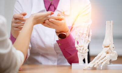 Female doctor examines patient's hand with bone models in medical rheumatology office