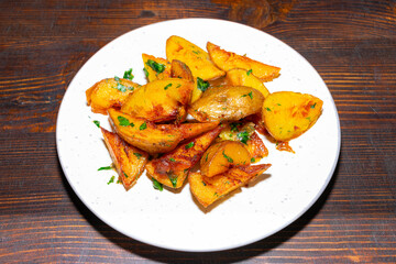 Golden roasted potatoes with herbs served on a white plate against a wooden background