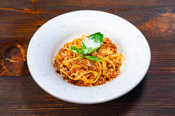 Delicious spaghetti topped with cheese and basil served in rustic bowl on wooden table