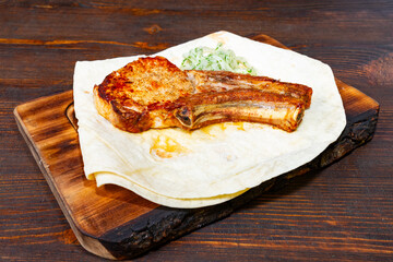 Juicy pork ribs served on flatbread with fresh toppings on wooden cutting board