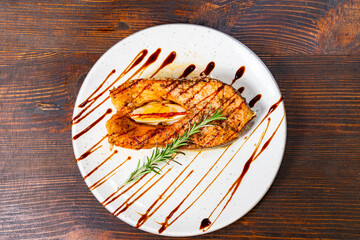 Grilled salmon fillet garnished with herbs and sauce served on a white plate