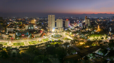 Fototapeta premium Aerial night views of a brightly illuminated central roundabout and surrounding cityscape in Thai Nguyen city, with traffic light trails.