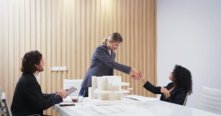 Architects concluding a meeting with a friendly handshake in a modern office. A scale model of a building is on the table, symbolizing teamwork, successful project collaboration. - Powered by Adobe