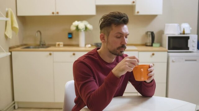 A 30-year-old man enjoys a casual meal and drink in his kitchen, captured in a natural, unposed moment. Authentic and relatable everyday scene perfect for lifestyle and food content