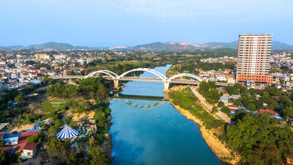 Aerial view of the Ben Tuong Bridge, an arch bridge spanning the Cau River in Thai Nguyen city, with its reflection in the water.