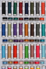 A top-down shot of a large assortment of colorful sewing threads neatly arranged in a white plastic storage box