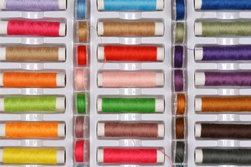A top-down shot of a large assortment of colorful sewing threads neatly arranged in a white plastic storage box
