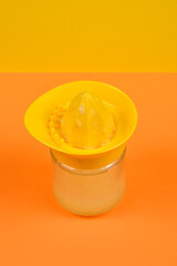 A bright yellow manual citrus juicer sits atop a glass jar filled with freshly squeezed lemon...