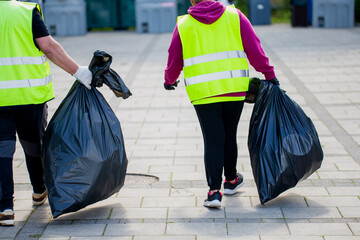 people in reflective safety vests carrying black garbage bags cleaning city streets during...