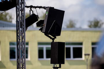 outdoor stage lighting and speaker setup at live event concert or festival professional audio visual equipment mounted on truss with school building in background sound system preparation concept