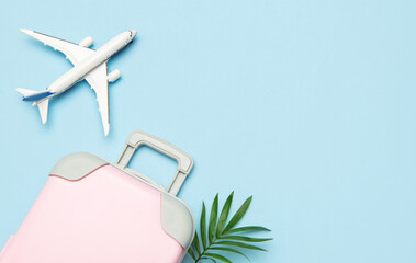 Pink suitcase, airplane model, and palm leaf on pastel blue background for travel concept