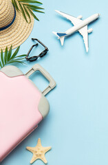 Pink suitcase, airplane model, sunglasses and straw hat on blue background with copy space