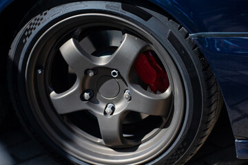 close up of modern alloy wheel with performance tire and red brake caliper on dark blue sports car...