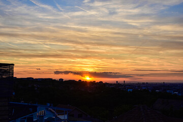 Sunset above city silhouette, sky in gray to orange tones