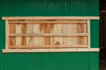 Wooden panel window frame on corrugated green metal wall exterior.
