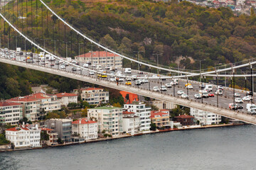 The Bosphorus Bridge, spans a body of water, packed with vehicles under an overcast sky in...