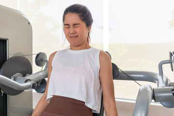 Asian woman pushing through pain, struggling face holding triceps arm workout at gym.
