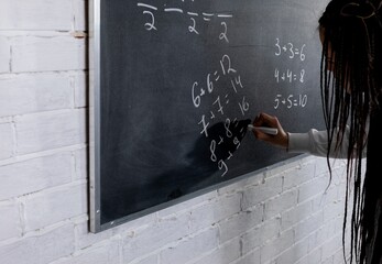 A teacher is diligently writing on a chalkboard in a classroom environment, engaging with students