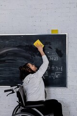 An empowered individual in a wheelchair cleans a blackboard, showing determination and achievement