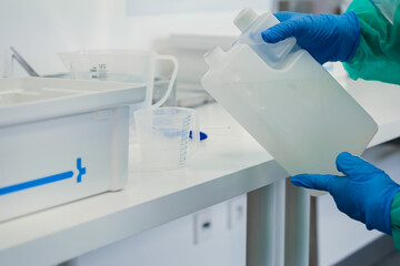 Healthcare professional in blue protective gloves pours liquid from large container, representing...