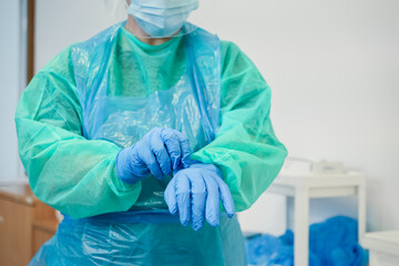Healthcare professional donning blue medical gloves, wearing personal protective equipment,...