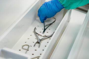 Professional gloved hand carefully places sterile surgical instruments into a white tray, ensuring...